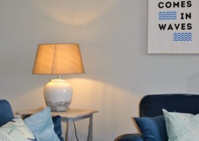 Lamp on table between sofas. Picture on wall reads It Comes In Waves