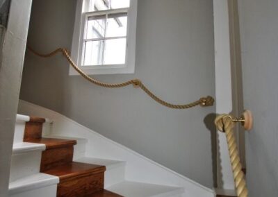 Wooden staircase curving to the left, rope bannister loops past window