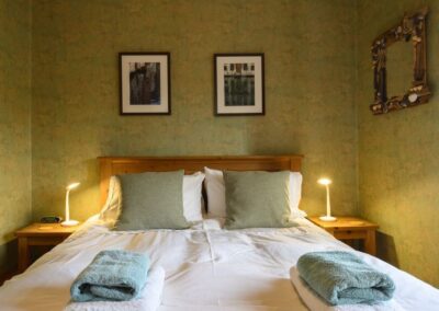 Double bed with bedside tables and lamps. Paintings above bed and mirror to right.