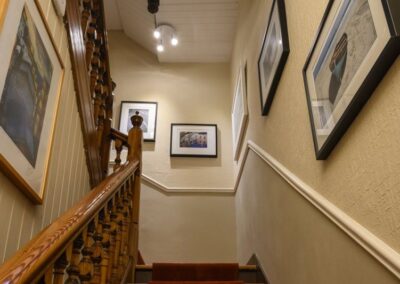 View up staircase which has framed paintings and photographs on either side and at the top
