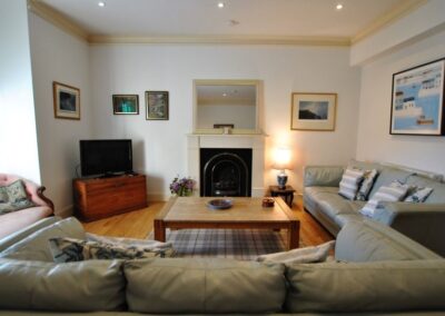 Photo of lounge taken from behind leather sofa, looking towards a fireplace. To the left is a TV and to the right another matching leather sofa.