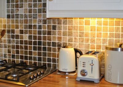 Kettle, toaster and bread bin next to gas hob, against a tiled splashback