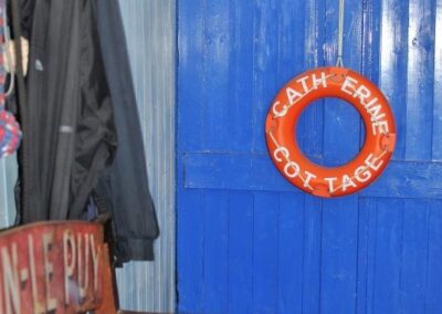 Blue front door with orange life ring hanging on the back that reads Catherine Cottage in white capital letters