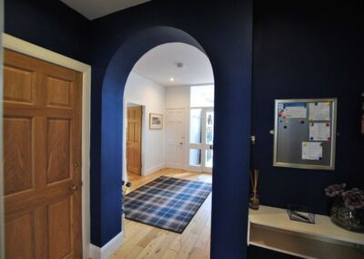 View through arch, painted a deep blue, towards the entrance hall with wooden floor and tartan rug
