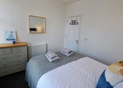 View across bed towards chest of drawers, wall-mounted mirror and door.