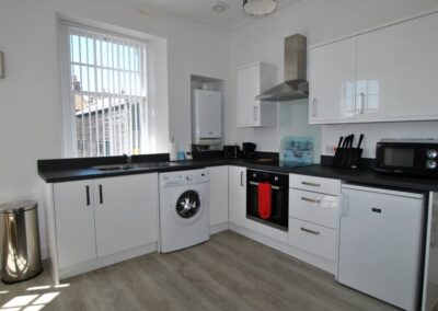 White kitchen units with black worktops. There is a washing machine next to the sink