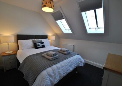 Double bed beneath a sloped ceiling with two windows