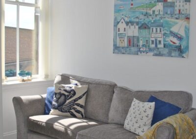 Grey sofa with coastal painting above, next to large, bright window