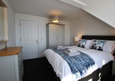 Chest of drawers on left, opposite large bed. A grey wardrobe sits to the right of the door.