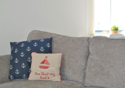 Grey sofa with two cushions. One is navy blue with white anchors, the other has a red boat with the words You float my boat.