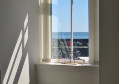 Light pouring in through a tall window with views to the harbour and sea beyond