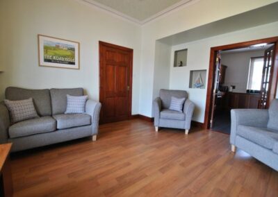View across lounge. Double sofa next to a door, with an armchair between that door and open double doors