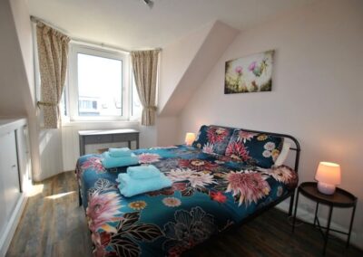 Double bed with floral linen, opposite wardrobe with mirrored doors
