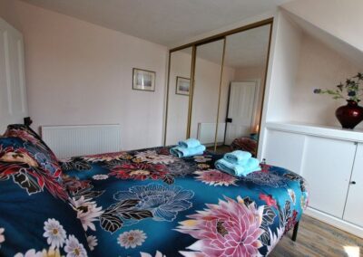 Double bed with floral linen, opposite wardrobe with mirrored doors