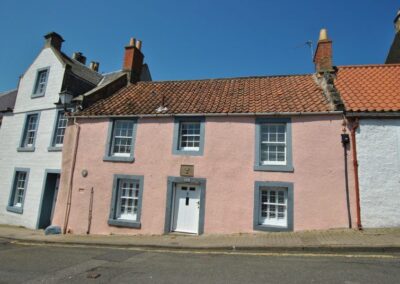 Pink, two storey cottage with red pantiles. White painted door with windows either side, and three windows on first floor.