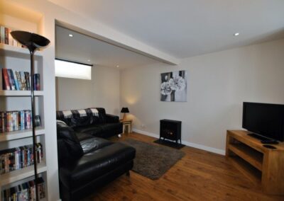 Wooden floor lounge with leather suite and TV on corner unit.