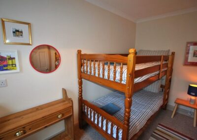 Wooden bunks with striped linen. There is a small lamp on a low bedside table.