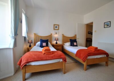 Single beds with wooden frames and white and orange linen side by side in a spacious, light bedroom.