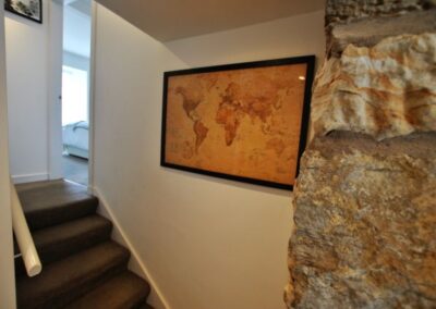 Sepia, landscape map of the world in a black frame hanging on the wall at the bottom of a short flight of stairs. There is an open door on the right at the top leading to a bedroom.