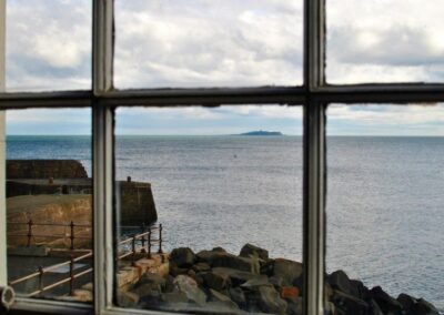 View out of window towards the Isle of May which lies low on the horizon, a lighthouse rise mid-island. To the left is the entrance to Cellardyke harbour.
