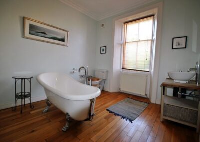 White roll top bath on wooden floor. The sink is a large white bowl on a wooden stand.