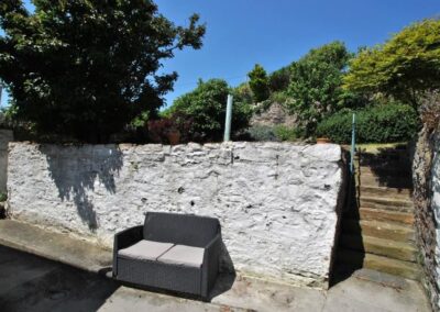 Outdoor sofa against a white painted wall. On the right, stone steps up to a grassed area.