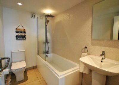 White bathroom suite with light walls and tiled floor. Lighting is sunk into the ceiling.