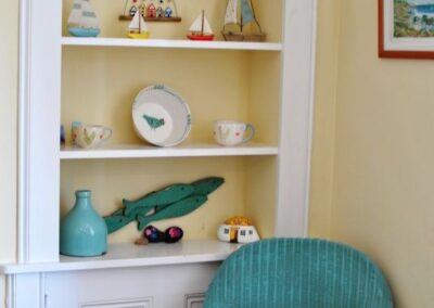 Alcove shelves with boats and fish ornaments. A turquoise wicker chair sits in front of the shelves.