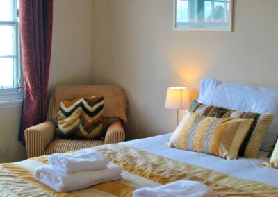 Golden, brown and white linen adorn a double bed and upholstered armchair.
