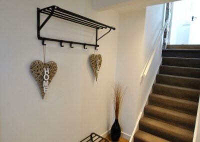 Boot rack on floor beneath wall-mounted coat and hat rack. Hanging from the coat hooks are two hearts that read HOME and LOVE. There are 10 steps up to the next level.