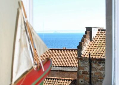 View of sea and rooftops from window. There is a model of a yacht on the windowsill.