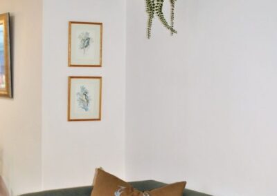 Brown stag design cushion on a green sofa, beneath a shelf with books, plant, picture and jug.