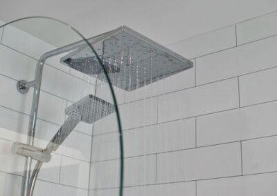 Square rainfall shower above the bath. The wall is tiled with white tiles.