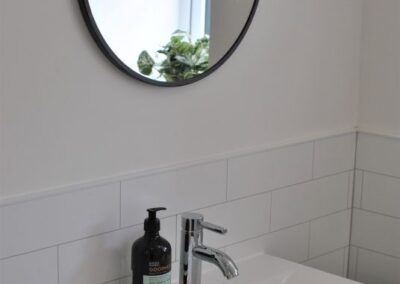 Oval mirror over a modern, white sink with mixer tap.