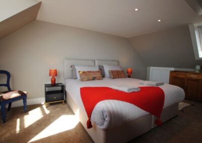 Superking bed with red throw in room with sloping ceiling. There are a couple of Velux-style windows in the roof.