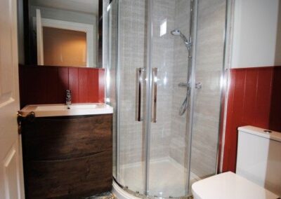 Quarter circle walk-in shower unit in corner of room. Floor has a patterned tile.