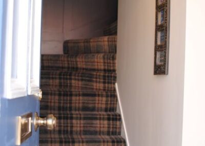 View through front door to staircase with yellow, black and red tartan carpet.