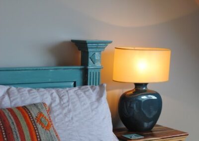 Close-up of pottery bedside lamp next to turquoise-framed bed.