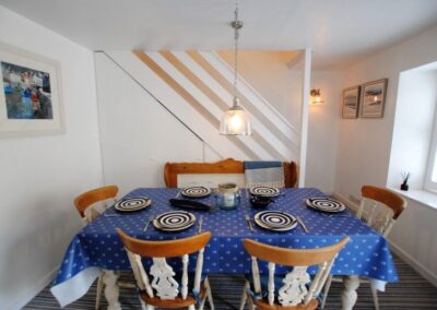 Dining table set for six. Beyond is a staircase leading up.