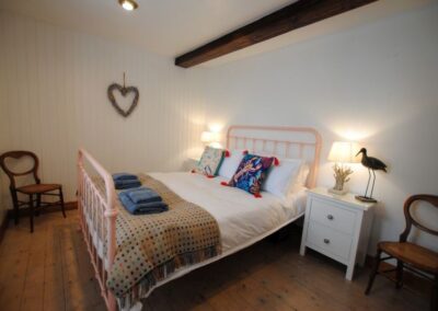 Pink-framed bed in wooden-floored bedroom. There is an exposed beam above the bed and a heart on the wall.