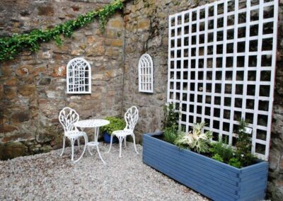 Gravel courtyard with white table and chairs. A white trellis reaches up the wall from a blue planter.