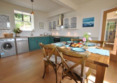 Large, bright kitchen with wooden dining table in the foreground set for four guests.