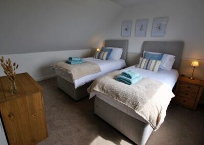 Twin single beds against a wall decorated with three framed artworks. Bedside tables with lamps next to each bed and a chest of drawers against an opposite wall.