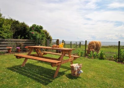 Picnic table in the garden. There is a cow grazing at the fence a few feet away.