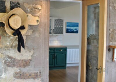 Straw hat with black ribbon hanging on a coat hook to the left of a door into the kitchen.