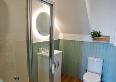 Walk-in shower on left. Beyond is a sink with circular, backlit mirror on the left and a lavatory straight ahead.