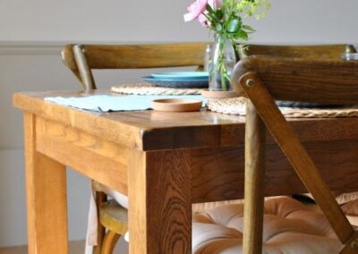 Close-up of wooden dining table and wooden chairs. The chairs have cushions tied to the seats.