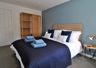 Double bed with white and blue linen. There is an oval bedside table with a metal angle-poise lamp either side.