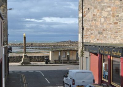 View past Indian restaurant towards the old market cross, a bus stop and rocks and sea beyond.