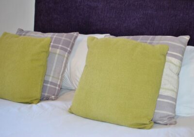 Close up of cushions on the master bed, these are yellow, light heather purple and white.
